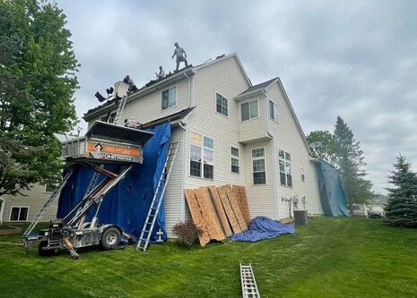 Ladders leaned up against a home with a new roof being laid.  