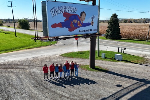 The Roofman USA team standing in front of the Roofman USA billboard in Saline